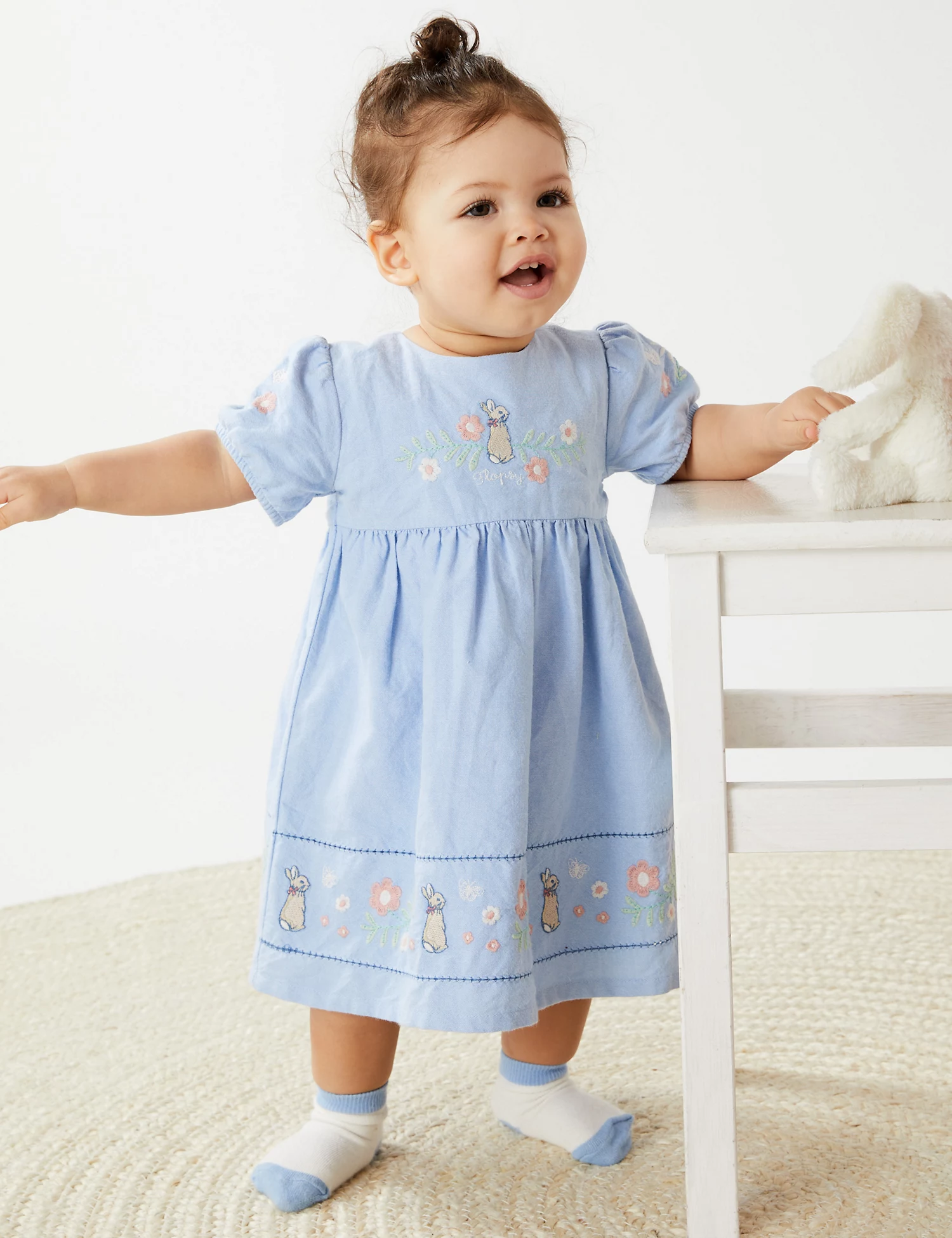 Child wearing a light blue dress embroidered with bunnies, flowers and a name