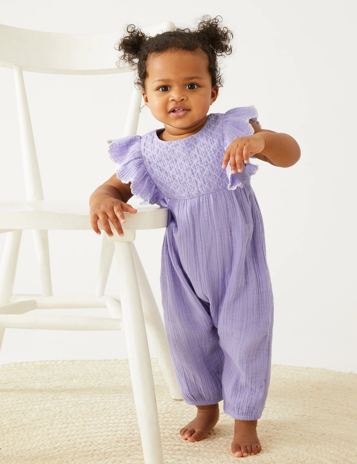 Baby wearing a lilac crinkle-gauze jumpsuit with ruffled cap sleeves