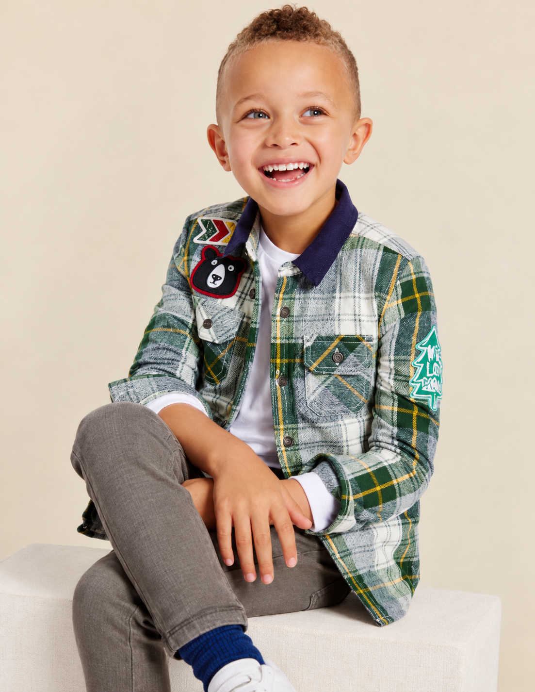 Boy wearing a green and yellow plaid patched overshirt over a white long-sleeve tee