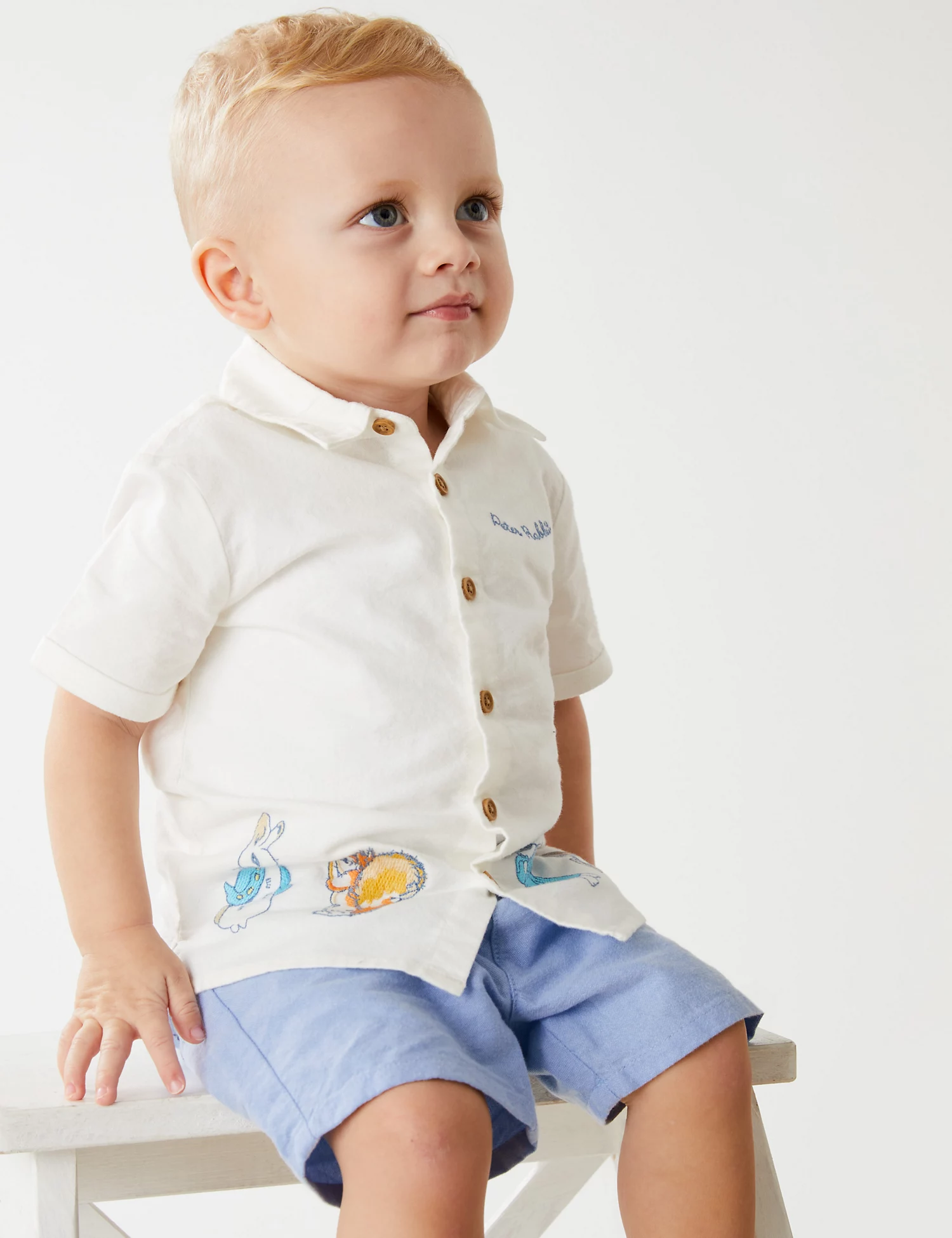 Child wearing a cream short-sleeve shirt with blue script and bunny prints, with periwinkle shorts