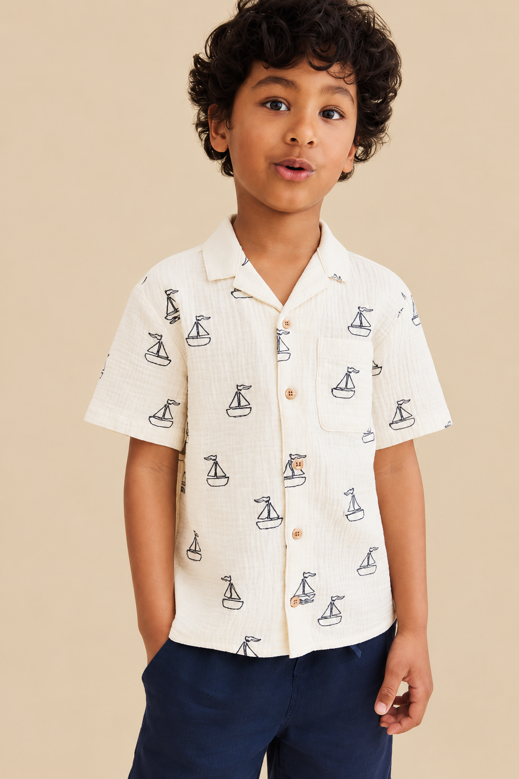 Boy wearing a cream short-sleeve shirt with navy sailboat print and navy shorts